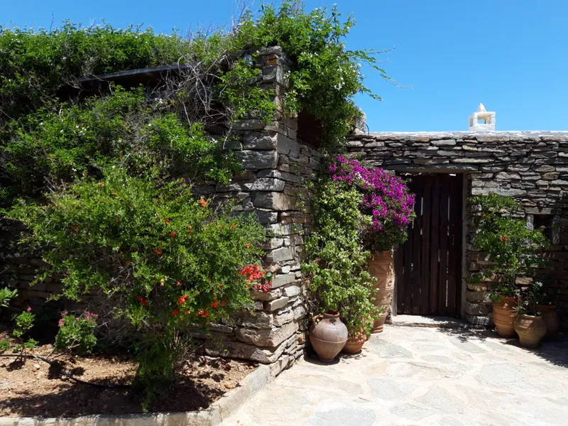 Dry-stone entrance wall draped in magenta bougainvillea and red flowering shrubs, with terracotta urns and a wooden gate