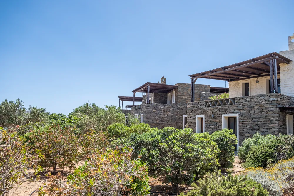 Stone villa exterior with multiple levels of terraces and Mediterranean shrubs under a clear blue sky
