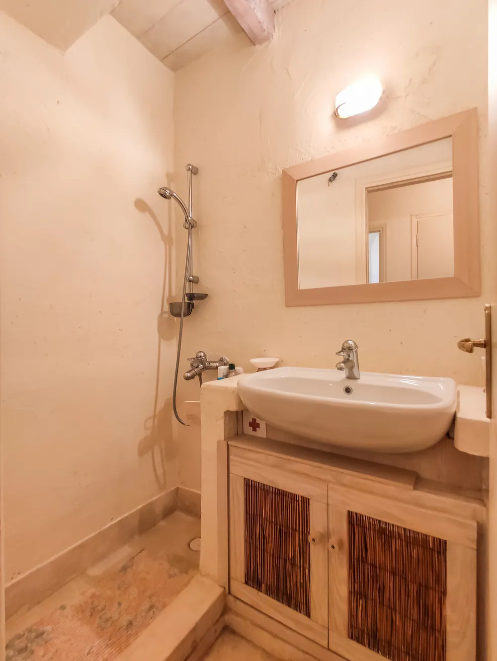 Guest bathroom with a wall-mounted shower, white basin on a wood-slat vanity, and a framed mirror