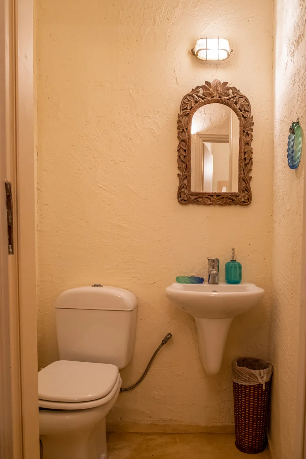 Compact WC with a pedestal basin, toilet, and a carved wooden mirror frame on a plastered wall