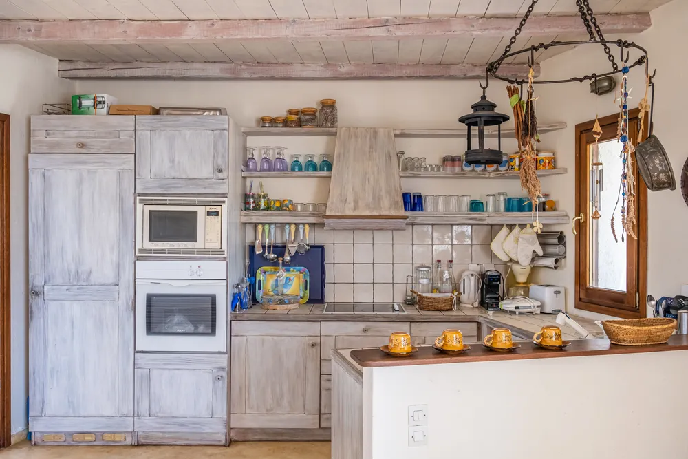 Rustic kitchen with limewashed wood cabinets, built-in white oven and microwave, open shelves, and white tiled splashback