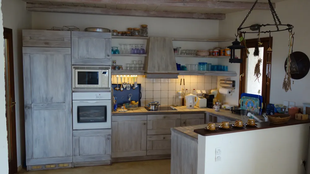 Kitchen from the dining side showing limewashed cabinets, open shelving, and a wood-beam ceiling