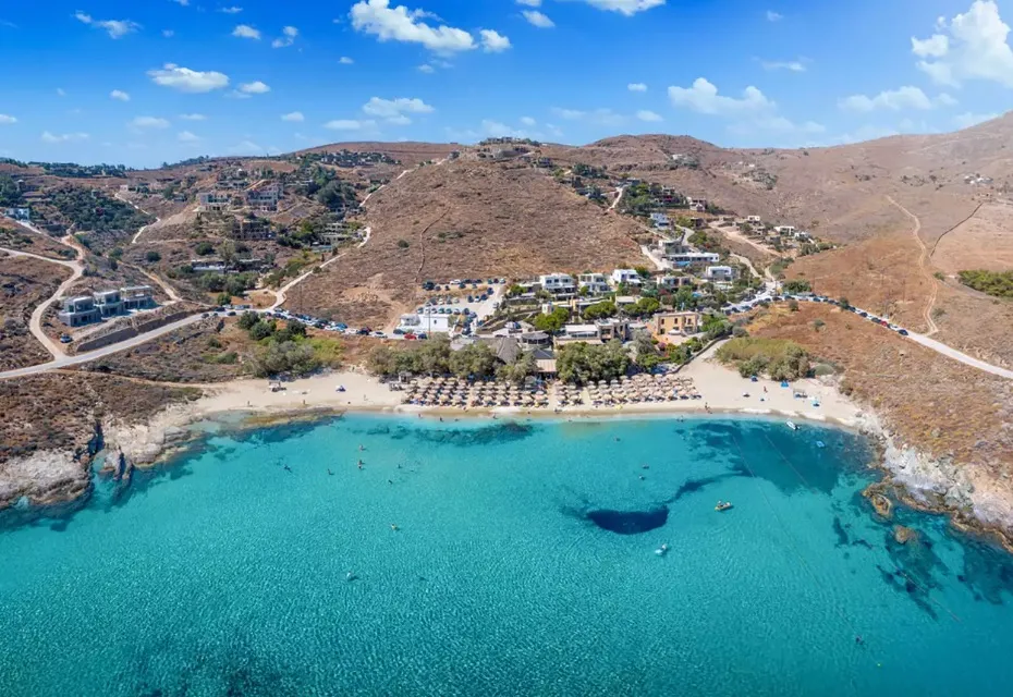 Aerial view of Koundouros bay, Kea, with turquoise water, sandy beach, and umbrella-covered shoreline