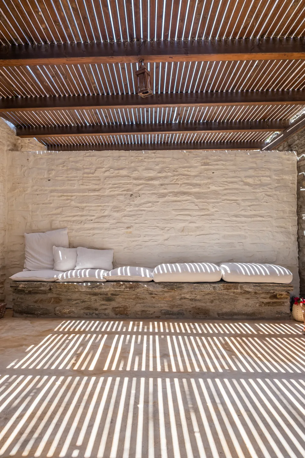 Wide white cushion daybed built into a whitewashed wall under a slatted pergola roof
