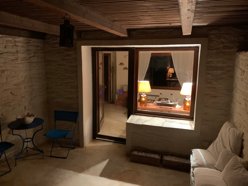 The living room at night, two warm table lamps lit beside the window, a hanging lantern, blue chairs, and a white sofa