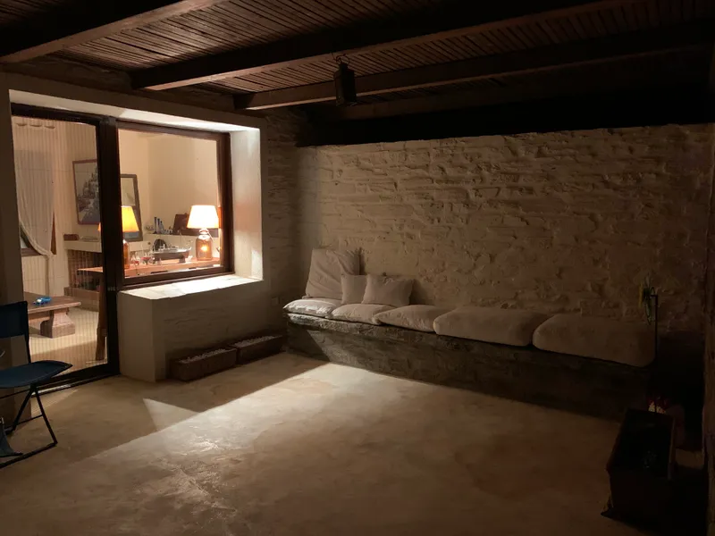 The stone living room in the evening, warm lamplight from the next room glowing over the built-in white-cushioned bench