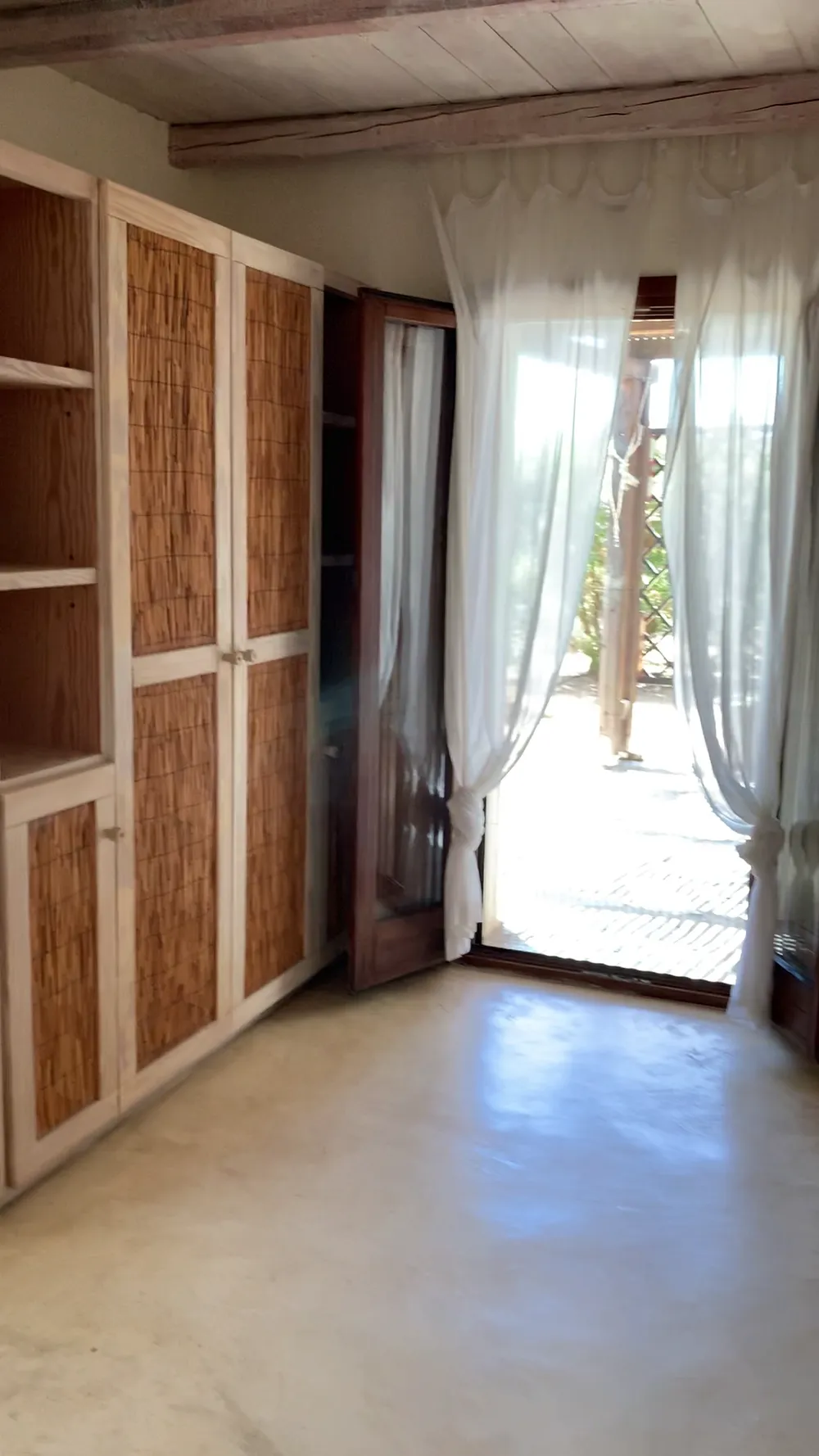 Master bedroom reed-fronted wardrobe beside a glazed door opening to an outdoor terrace with sheer curtains