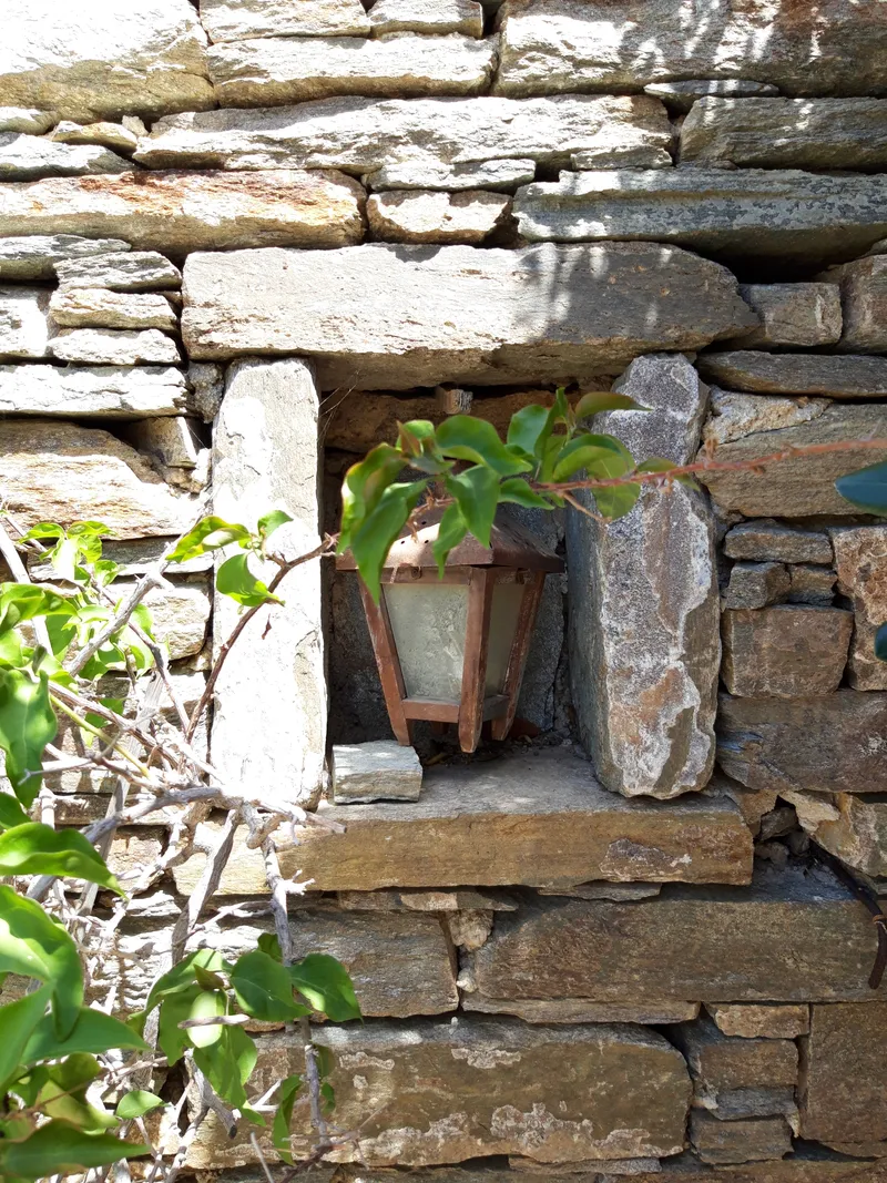 A rustic metal lantern set into a niche in the dry-stone wall, framed by climbing greenery